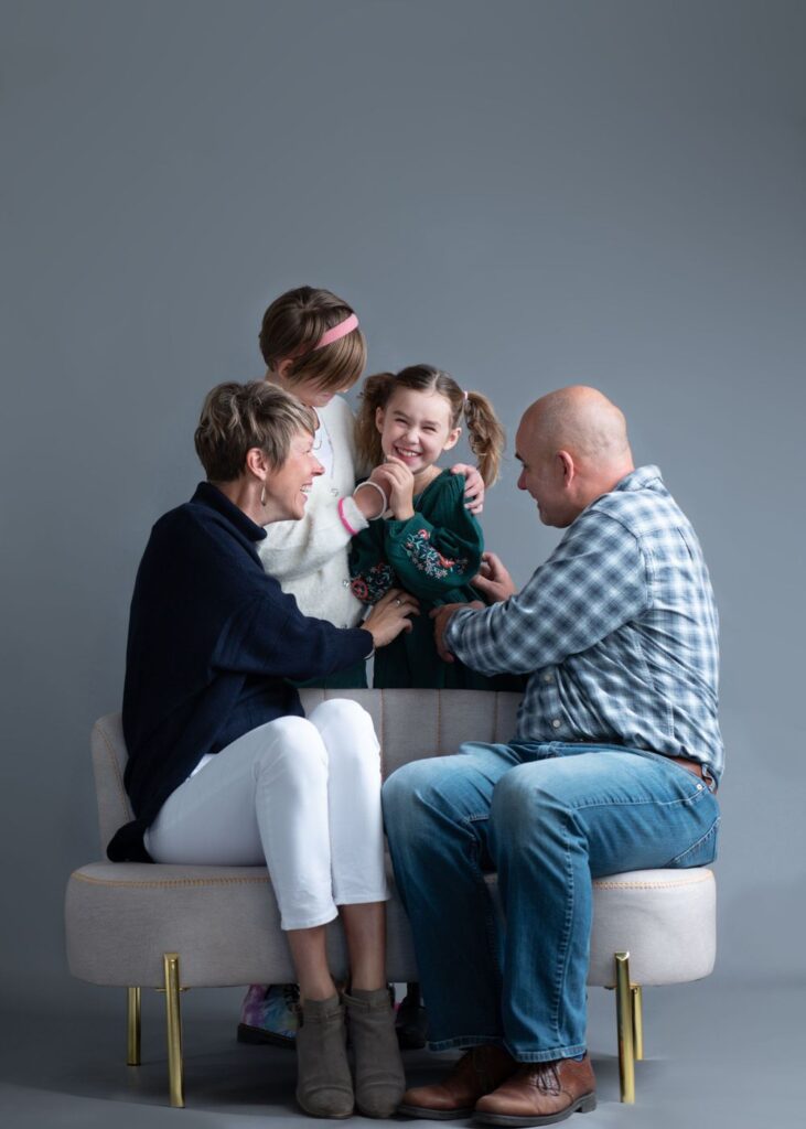 A joyful family moment: two adults and a young child sitting on a sofa, engaging lovingly with a smiling toddler held by one of the adults.