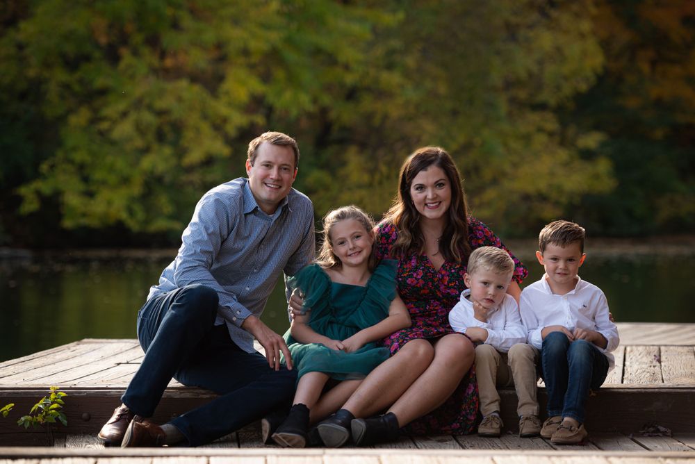 Family of five posing for a photograph on a wooden dock with autumn foliage in the background.