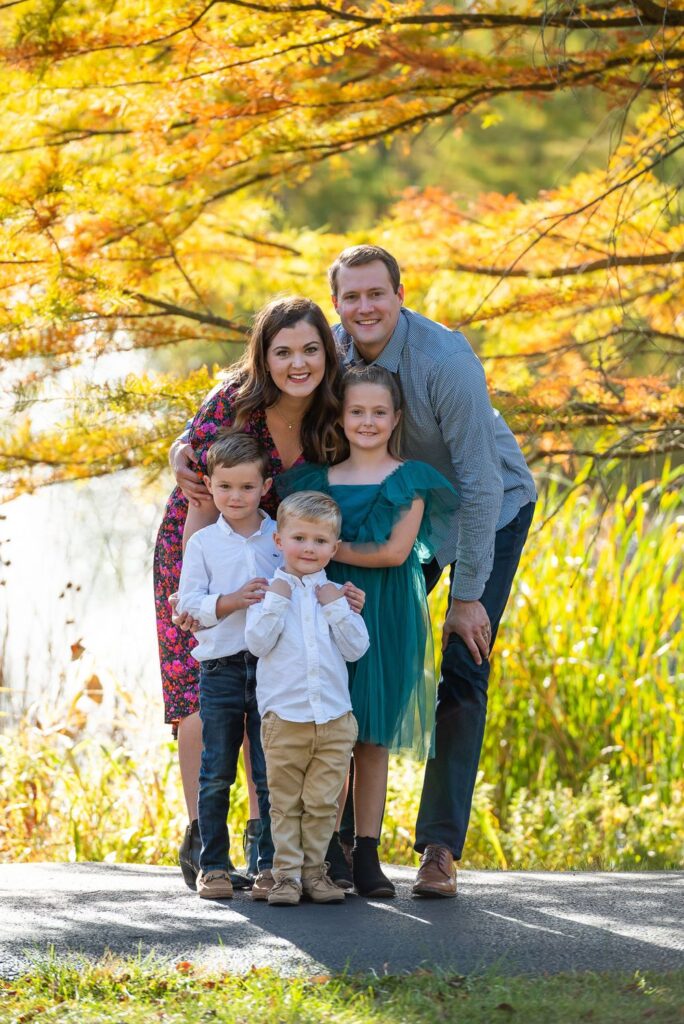 A happy family of five posing for a photo outdoors with autumn foliage in the background.