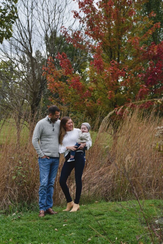 A family of three enjoying a moment together in an autumnal setting outdoors.
