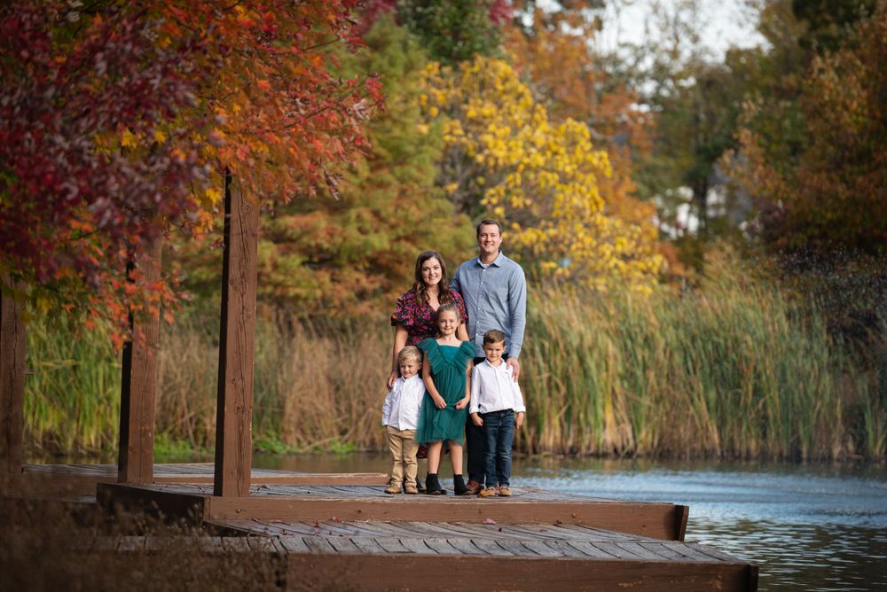 A family of five posing for a portrait on a wooden dock surrounded by autumn foliage.