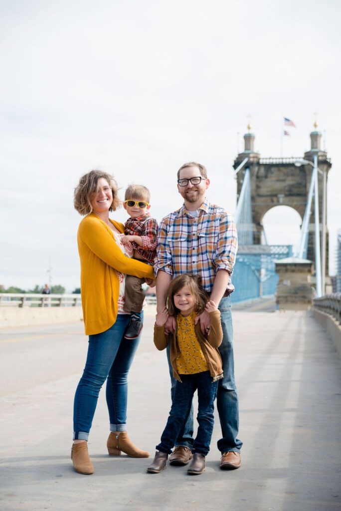 A family of four posing on a bridge with a suspension tower in the background.