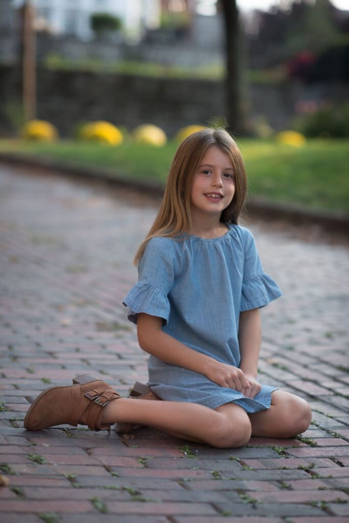 Young girl sitting on a brick pathway smiling at the camera.