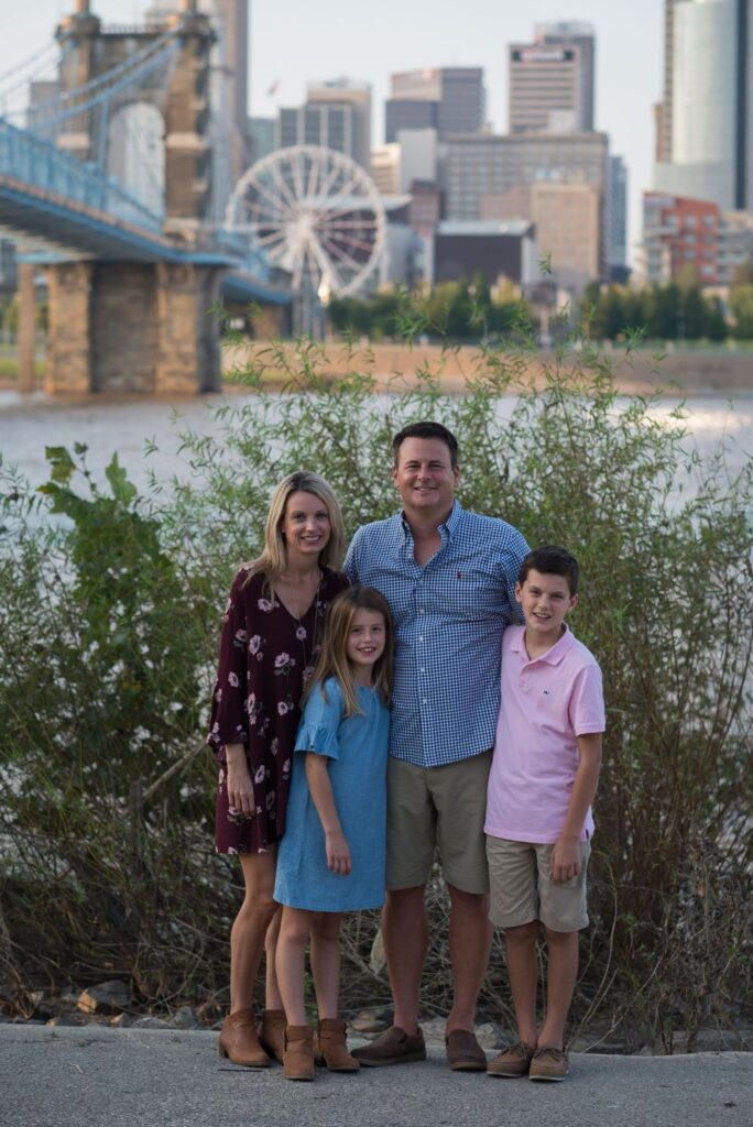 A family of four posing for a portrait with a bridge and a ferris wheel in the background.