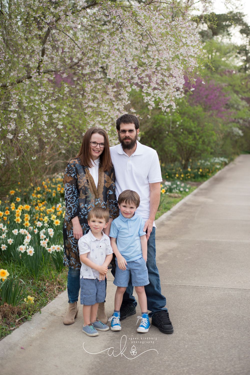 A family of four posing for a photo on a pathway surrounded by spring blooms.