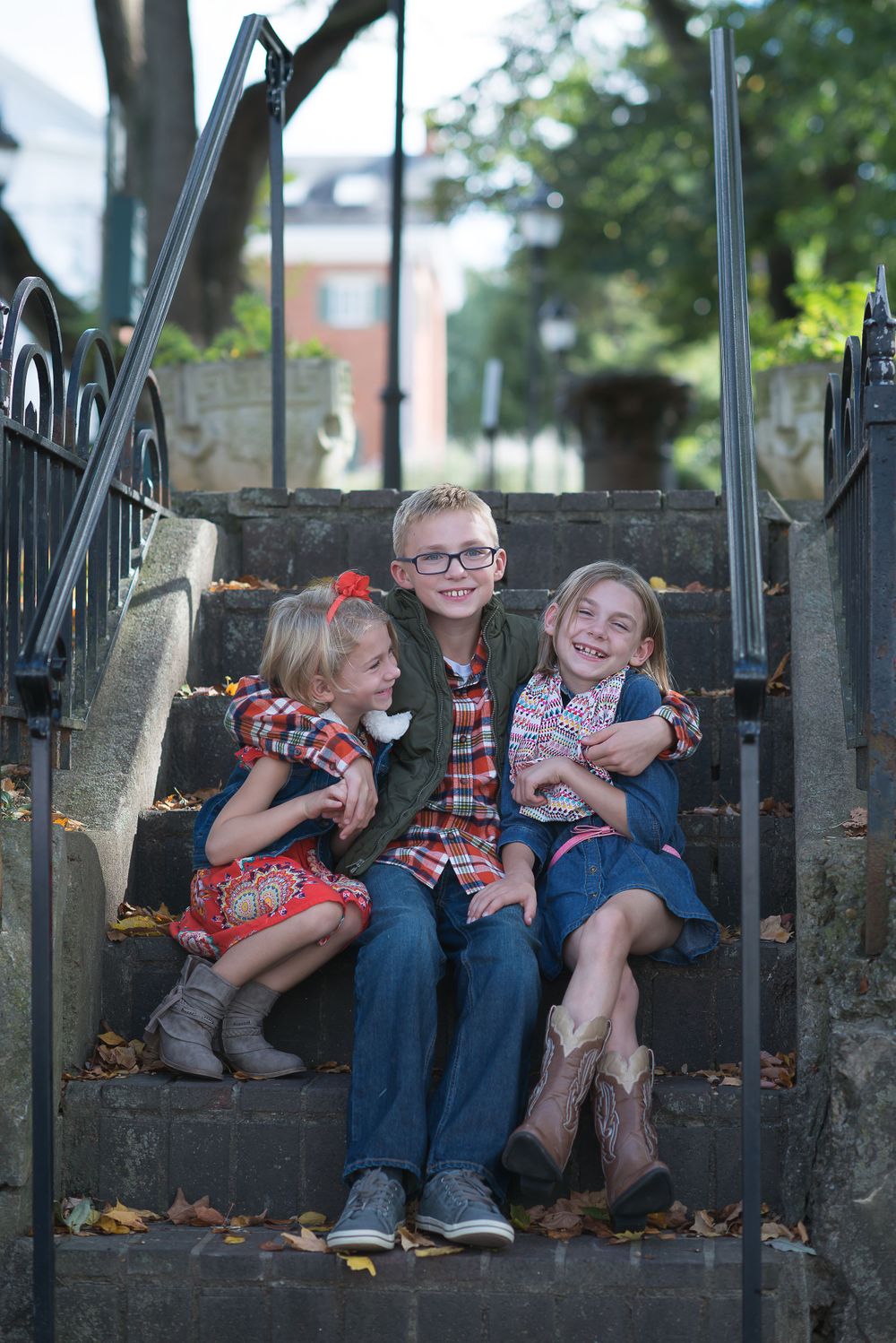 Three smiling children sitting together on outdoor steps.
