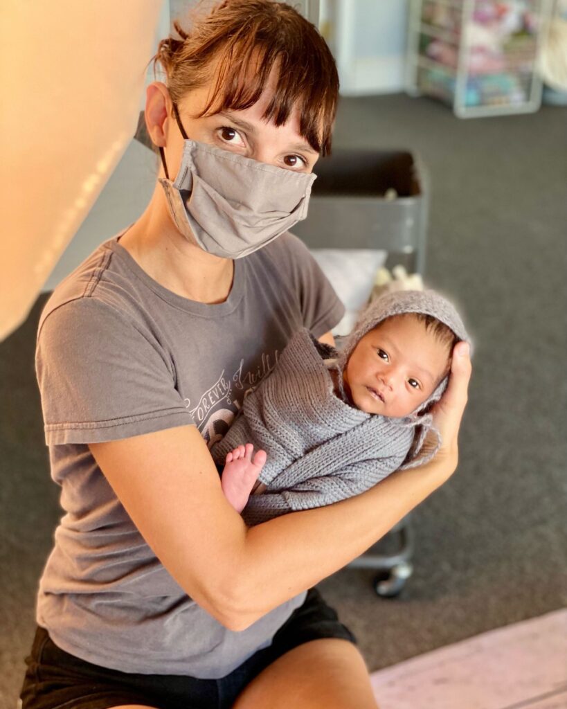 Woman behind the scene in a mask holding a swaddled newborn baby.