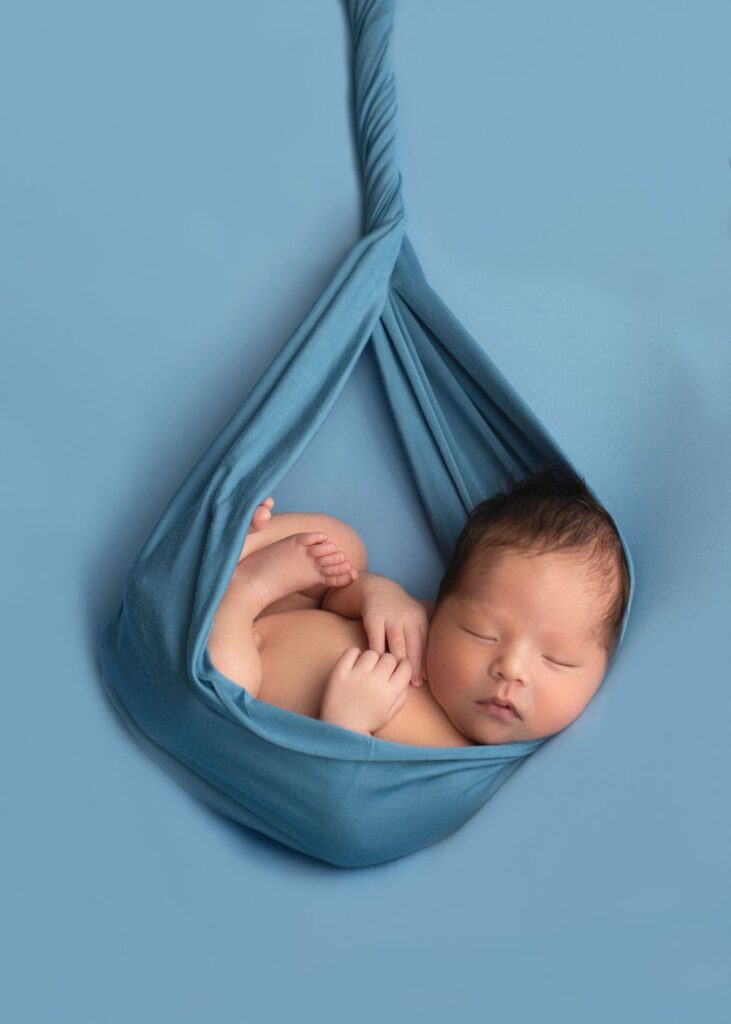 Newborn sleeping in a blue fabric hammock.