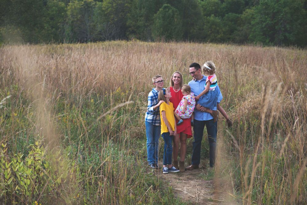 Family of four standing together on a nature trail among tall grasses.