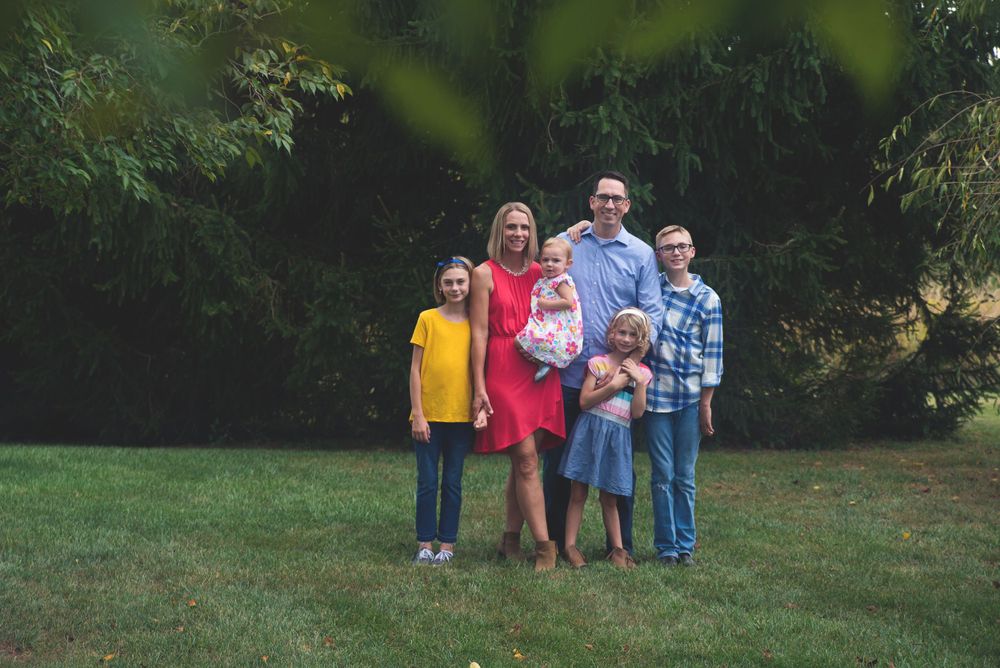 A family of five posing for a portrait in a park with greenery in the background.