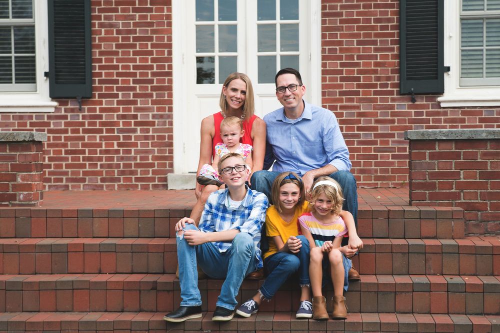 A family of five sitting together on brick steps in front of a house.