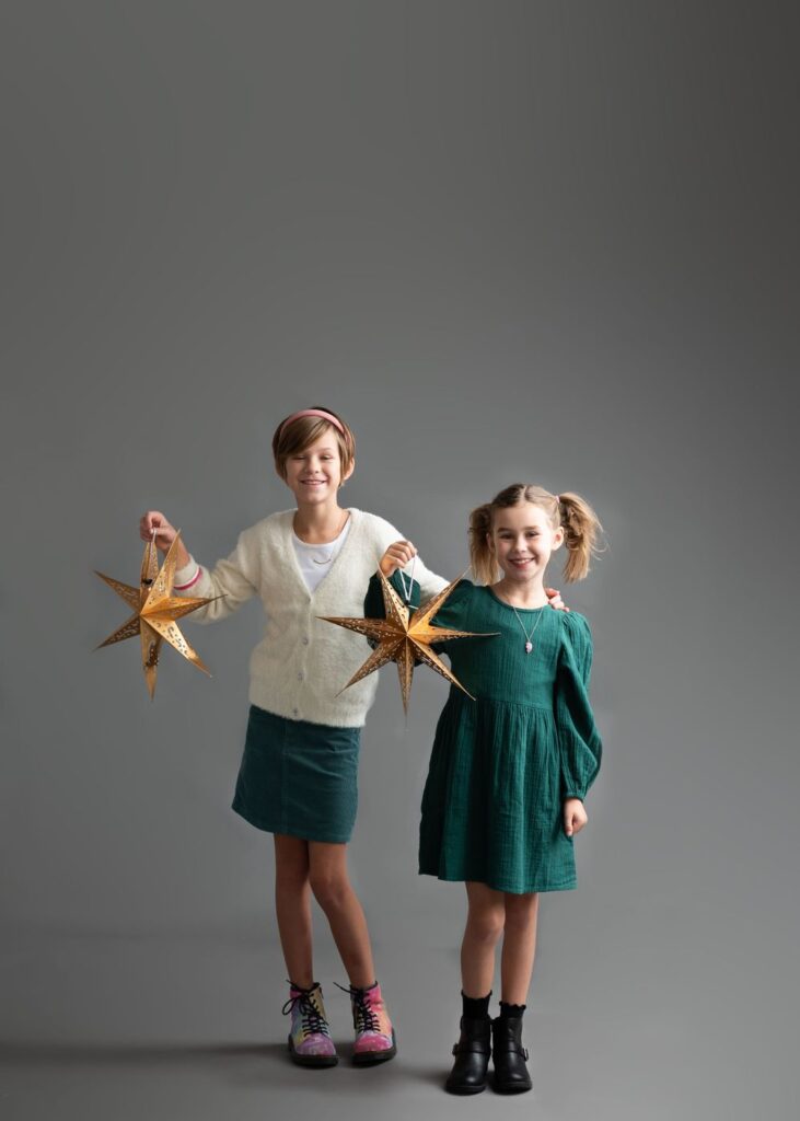 Two smiling children holding golden star-shaped ornaments against a gray background.