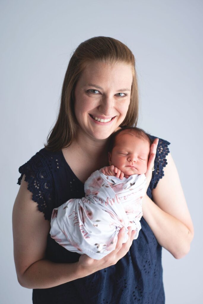 Woman smiling while holding a sleeping newborn baby.