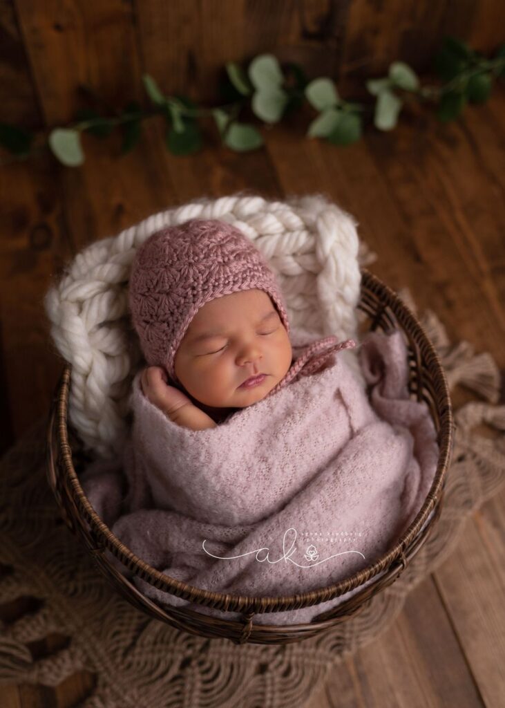 Newborn baby swaddled in pink, sleeping peacefully in a basket with a knit hat on.