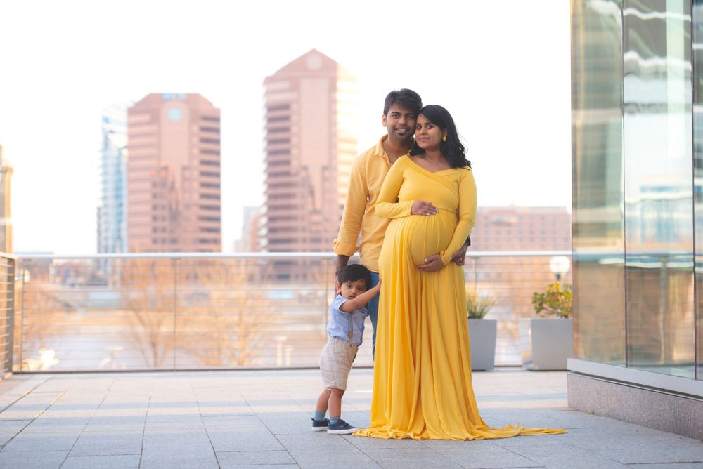 A family with a pregnant mother, father, and young child standing together outdoors in a city setting.