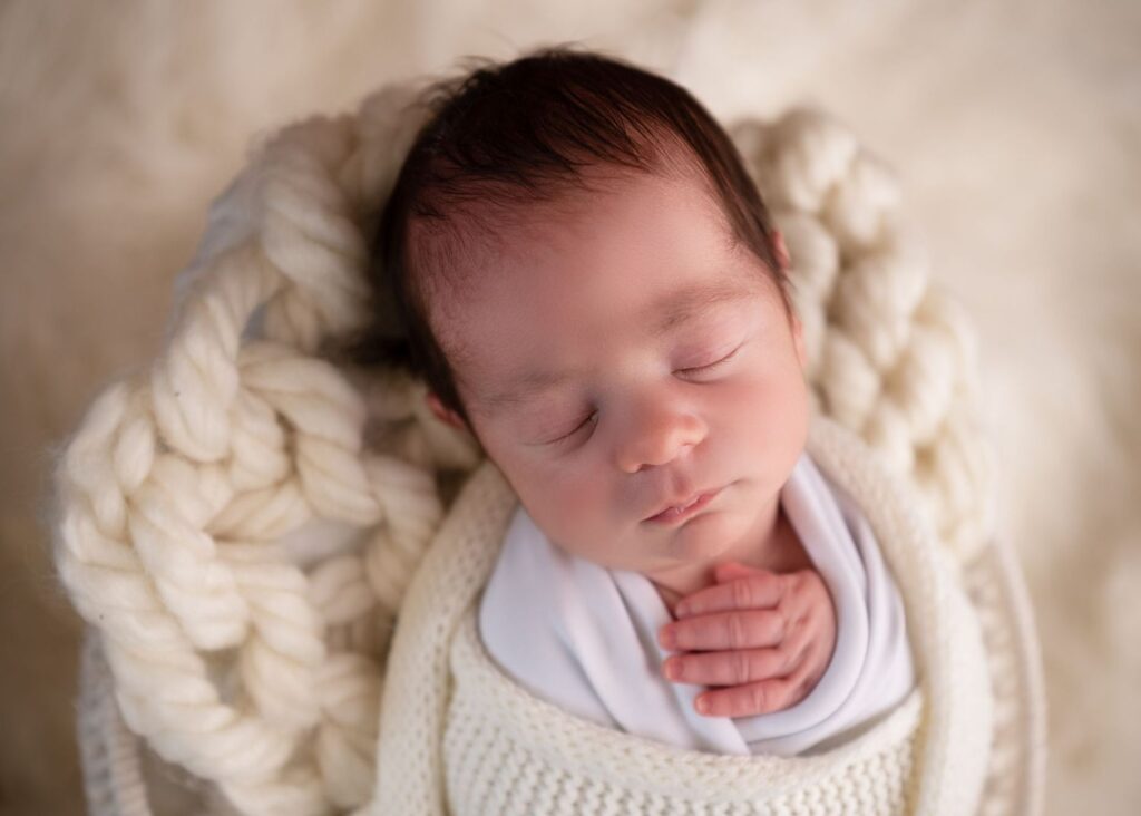 Newborn baby sleeping peacefully in a knitted blanket.