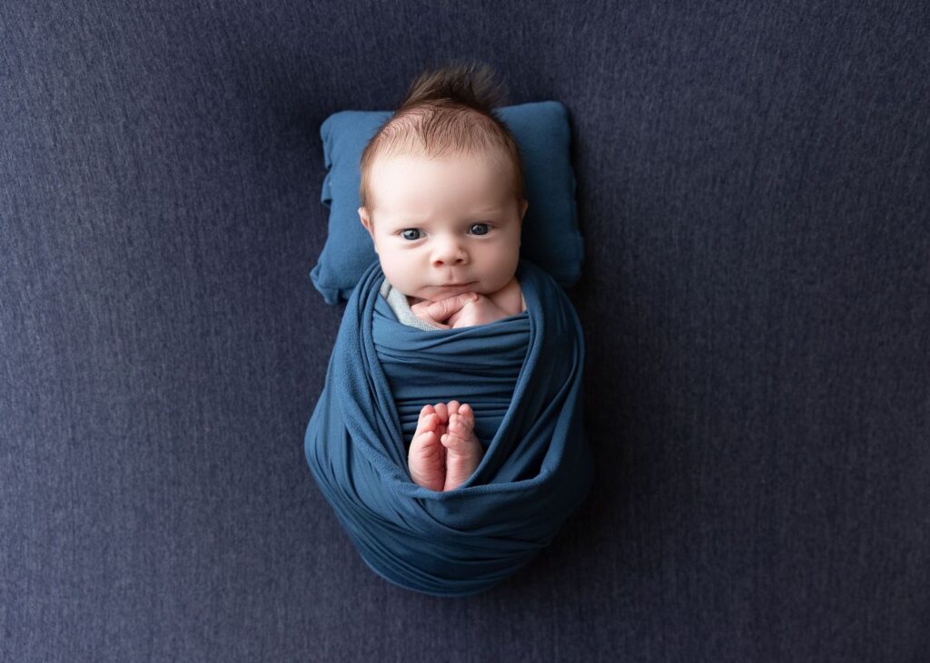 Swaddled newborn with tuft of hair lying on a blue blanket.