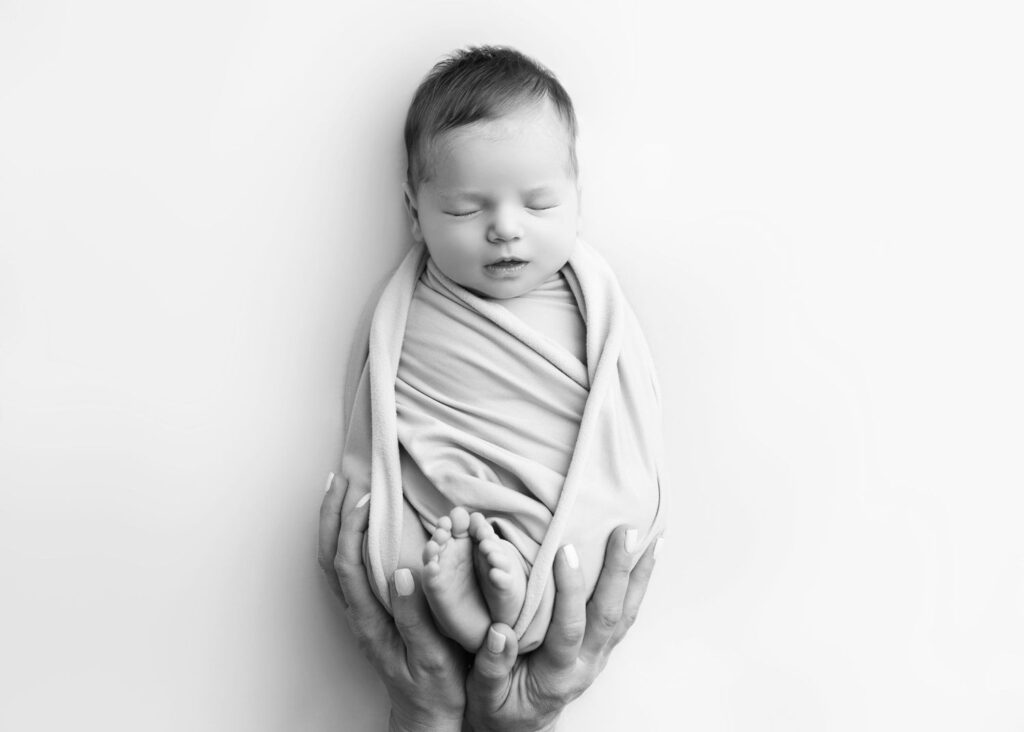 Newborn baby cradled in adult hands, swaddled in a soft cloth, peaceful in black and white.