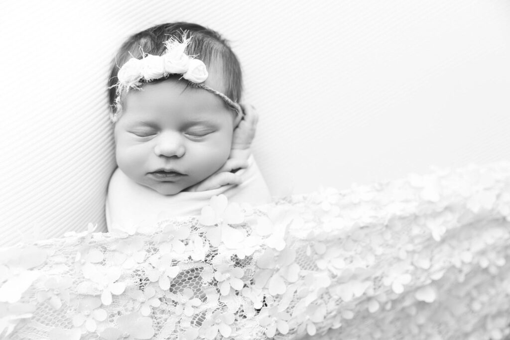 Newborn baby wrapped in a blanket, adorned with a floral headband, sleeping peacefully.