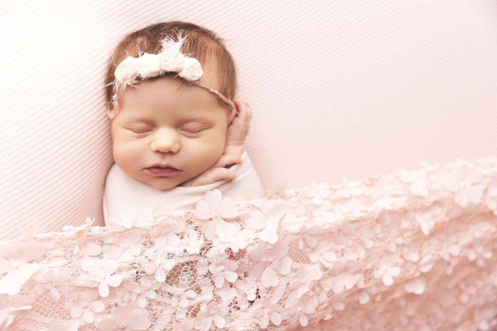 Newborn baby sleeping peacefully wrapped in a soft fabric with a floral headband.