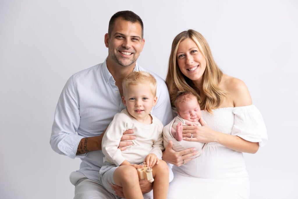A family portrait featuring a smiling couple with a toddler and a newborn baby.