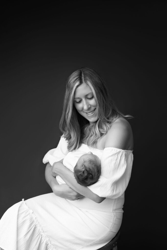 A black and white portrait of a smiling woman holding a newborn baby.