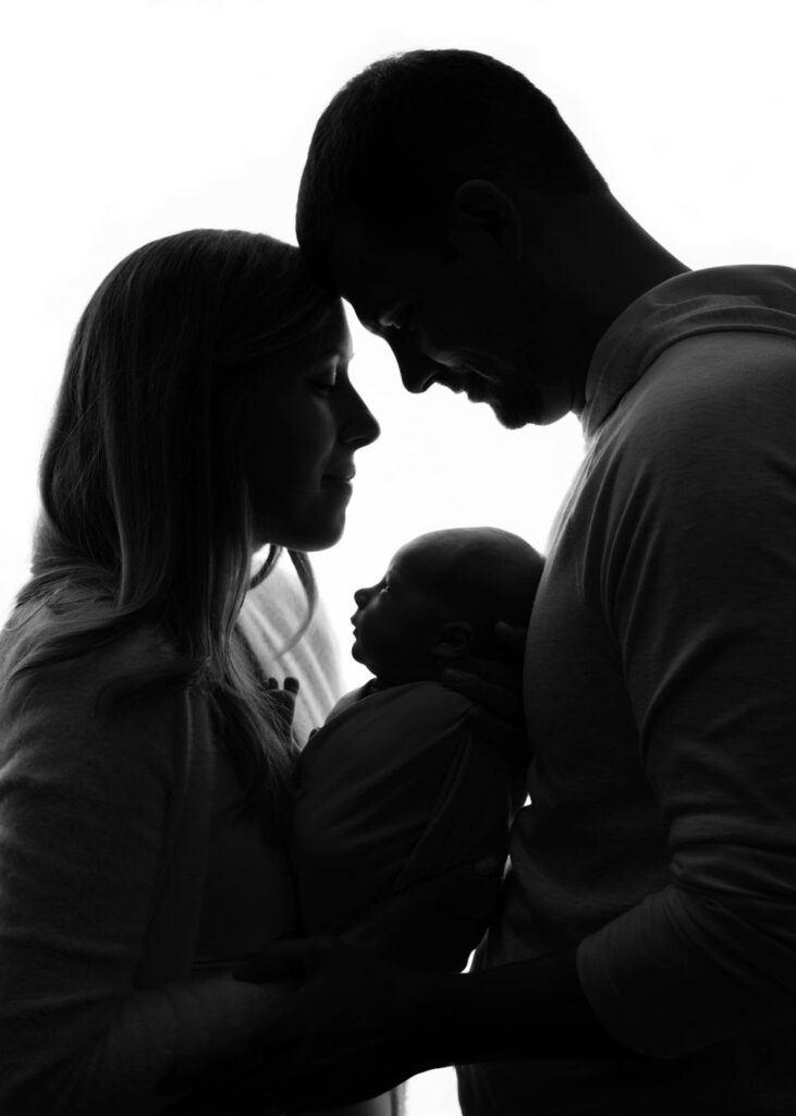 Silhouetted image of a couple gazing at each other, holding a baby.