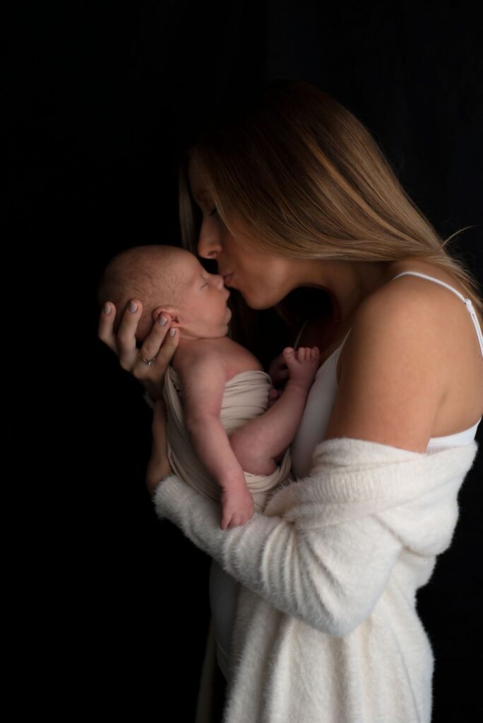 A mother affectionately kissing her newborn baby's forehead.