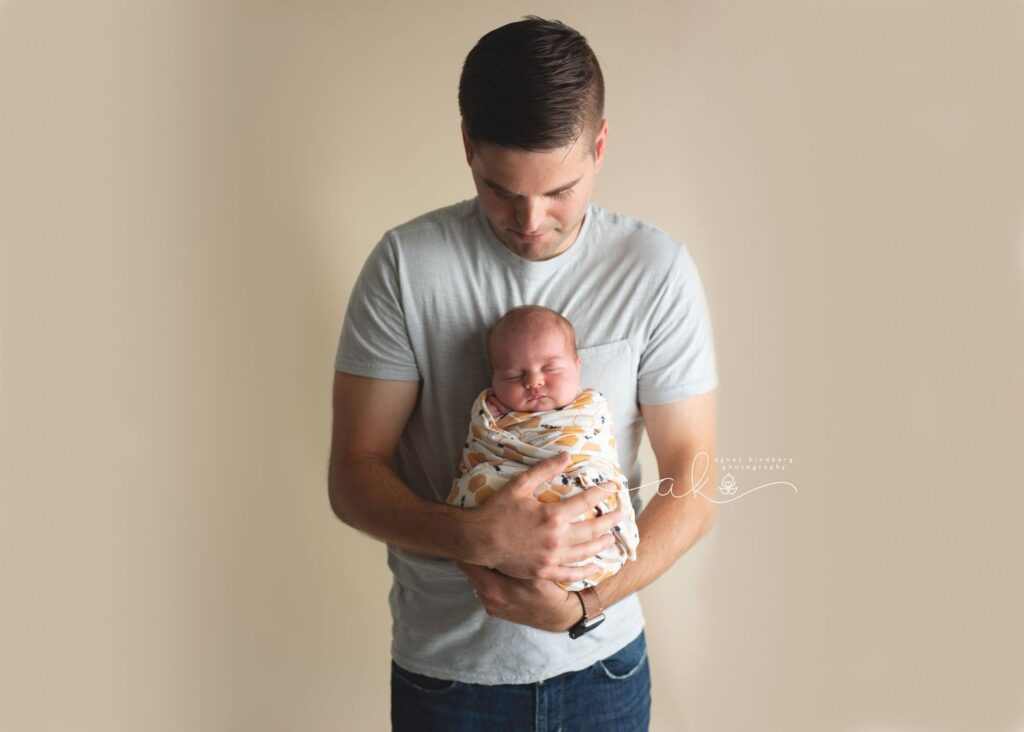 Man holding a sleeping newborn baby wrapped in a blanket.