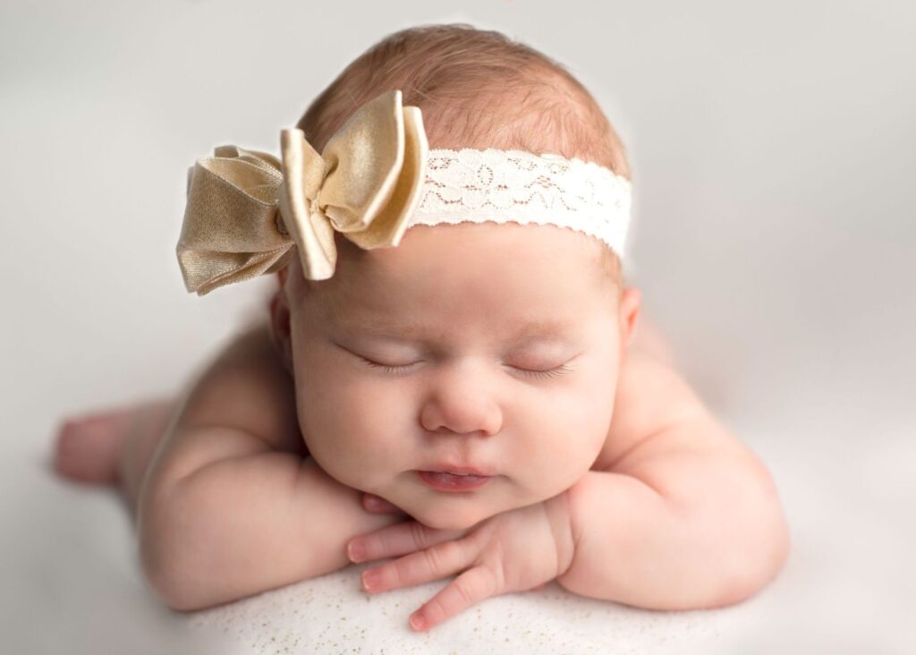 Newborn baby with a golden bow headband sleeping peacefully.