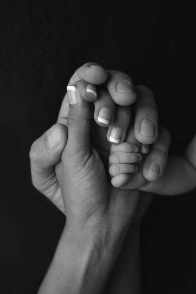 An adult hand gently holding a child's hand against a dark background.