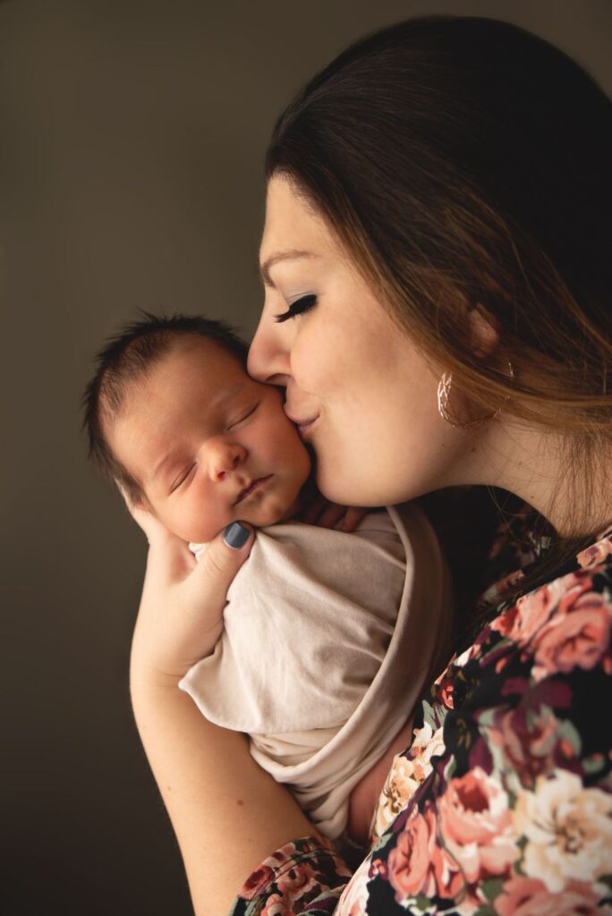 A mother tenderly kisses her newborn child's forehead.