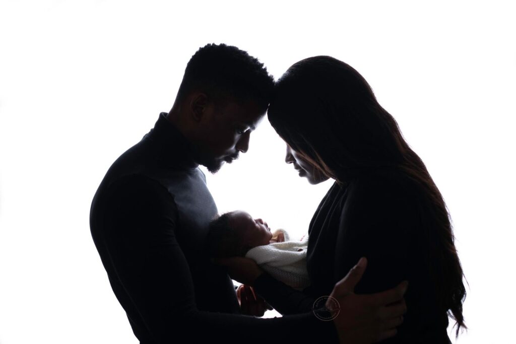 Silhouetted image of a couple affectionately looking at their baby.