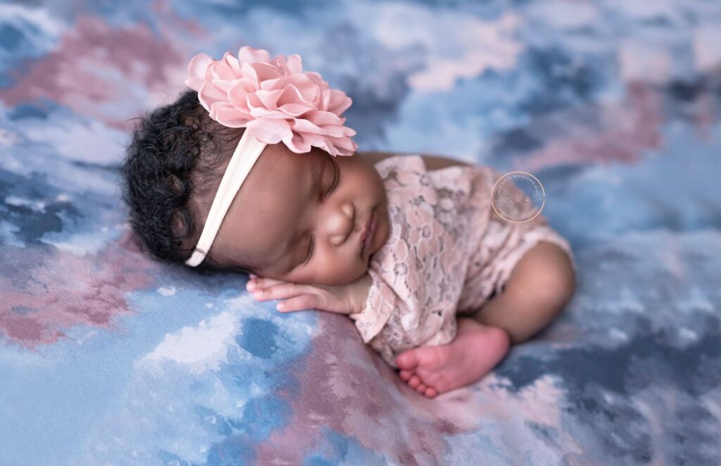 Newborn baby resting on a colorful backdrop with a flower headband, next to a translucent bubble.