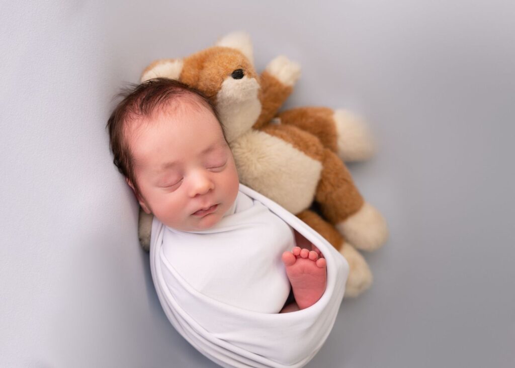 Newborn baby sleeping peacefully with a plush toy fox.