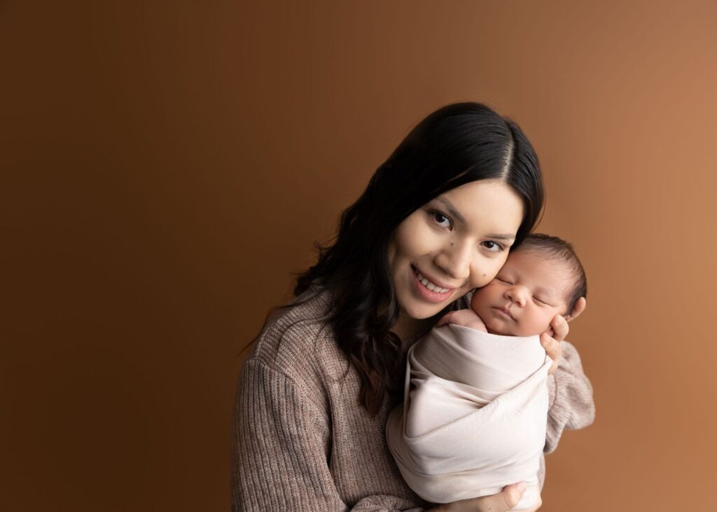 Woman holding a sleeping newborn baby against a brown background.