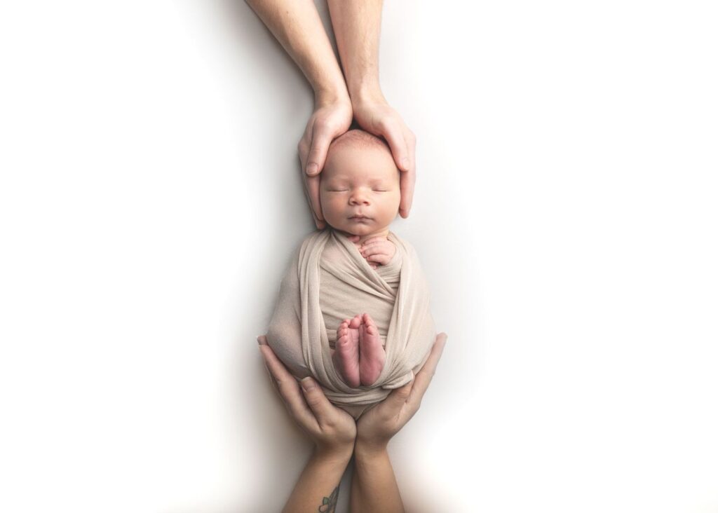 Newborn cradled in hands against a white background.