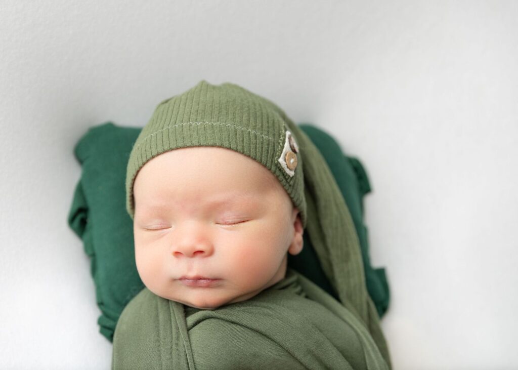 Newborn baby wrapped in green cloth and wearing a matching hat, sleeping peacefully.