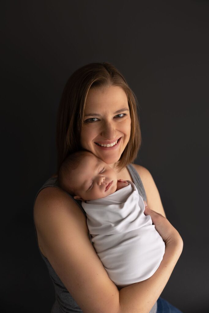 A smiling woman holding a sleeping infant against her chest.