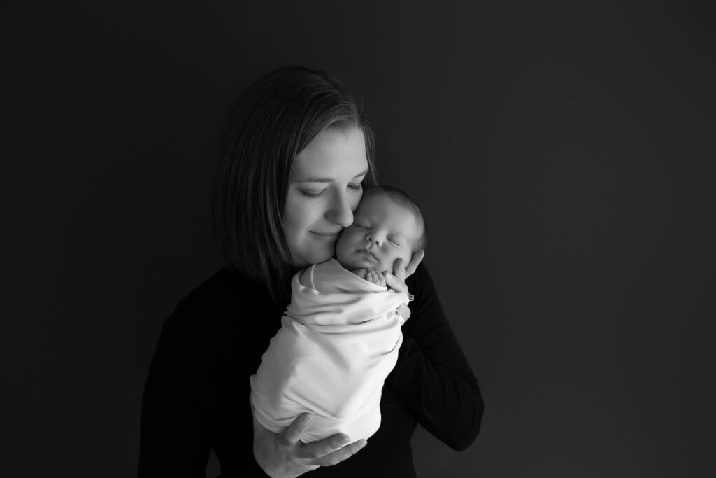 A mother affectionately holding her newborn baby, both captured in a serene black and white portrait.